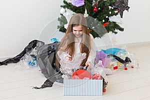 Environmental protection and pollution concept. Sad child carrier box with plastic trash over christmas tree background.