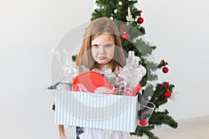 Environmental protection and pollution concept. Sad child carrier box with plastic trash over christmas tree background.
