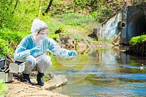 Environmental scientist with a flask takes a sample of water at the site of industrial discharge