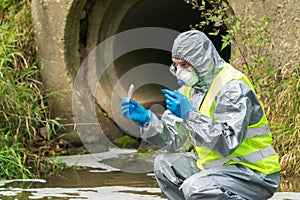 Environmental specialist in a protective suit and mask took a sample of wastewater water to study the level of pollution