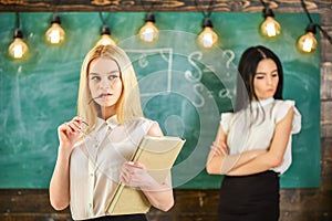 Envy and competition concept. Girl jealous of success of classmate in classroom, chalkboard on background. Woman with photo