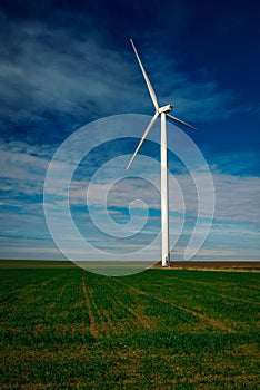 Eolian turbine with big propellers used to produce green energy seen from a wheat field in the spring