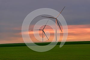 Eolian turbines used to produce green energy seen from a wheat field in the spring