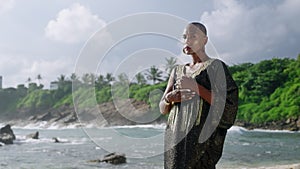 Epatage androgyne gay black man in luxury gown poses on scenic ocean beach. Non-binary ethnic fashion model in long posh