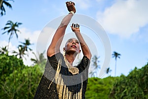 Epatage lgbtq black male posing with hands up on camera on scenic palm tree location. Non-binary ethnic fashion model in