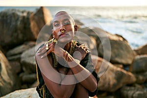 Epatage lgbtq black man poses on scenic ocean beach looks at camera demonstrates jewellery . Androgynous ethnic fashion