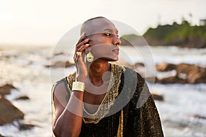 Epatage lgbtq black man poses on scenic ocean beach looks at camera demonstrates jewellery . Androgynous ethnic fashion