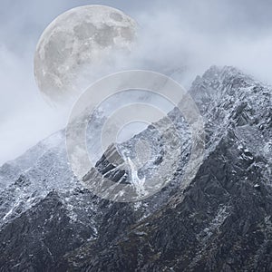 Epic digital composite image of Supermoon above mountain range giving very surreal fantasy look to the dramatic landscape image photo