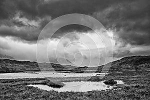 Epic dramatic black and white landscape image of Loch Ba on Rannoch Moor in Scottish Highlands on a Winter morning