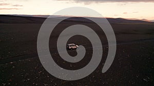 Epic Iceland Sunrise 4 Wheel Drive White Car Drives F-Road. Drone Follows Behind Vehicle Over Dirt Wide Martian Landscape