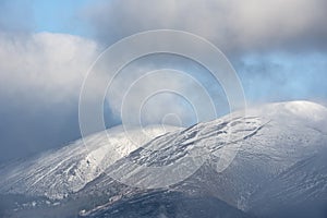 Epic landscape image of Skiddaw snow capped mountain range in Lake District in Winter with low level cloud around peaks viewed