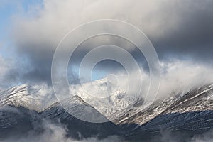 Epic landscape image of Skiddaw snow capped mountain range in Lake District in Winter with low level cloud around peaks viewed