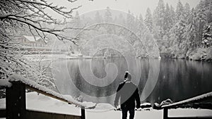 Epic shot of a lonely man walking towards partly frozen, mountain lake of Switzerland. Blausee in winter during snowfall