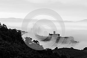 An epic view of St.Francis church in Assisi town Umbria above a sea of fog at dawn with trees and hills on the