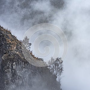 Epic Winter landscape image of view from Side Pike towards Langdale pikes with low level clouds on mountain tops and moody mist