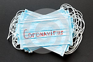 Epidemic background made of coronavirus word on heap of protective medical masks on black background. World quarantine concept