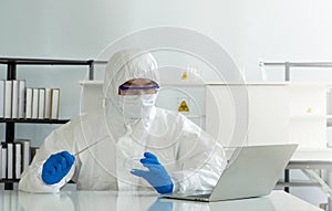 Epidemiological researchers in virus protective clothing look at  laptop computer screen while holding Inoculating Needle and