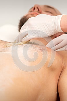 Epilation chest of a young male with the liquid wax paste in a beauty salon.