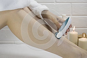 Epilation of legs at home. Young woman shaving her legs using an electric epilator. Woman epilate legs with electric epilator.