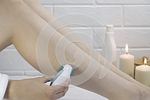 Epilation of legs at home. Young woman shaving her legs using an electric epilator. Woman epilate legs with electric epilator.