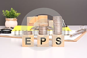 EPS text in wooden blocks with coins stacked in increasing stacks. Earnings Per Share concept