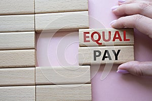 Equal Pay symbol. Wooden blocks with words Equal Pay. Beautiful pink background. Businessman hand. Business and Equal Pay concept