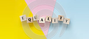 Equality banner word made withvwooden blocks over colorful pink, yellow, blue background, inclusion concept