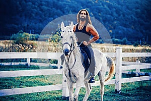 Equestrian and animal love concept. Rider on gray arabian horse in the field. Handsome bearded man riding horse at farm photo