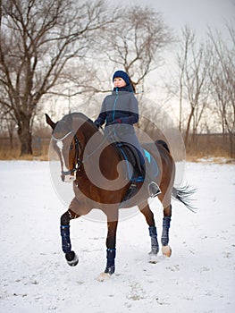 Equestrian country girl riding her bay horse in winter