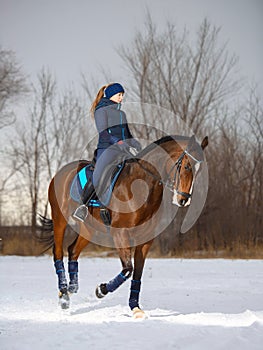 Equestrian country girl riding her bay horse in winter