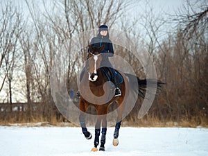 Equestrian country girl riding her bay horse in winter