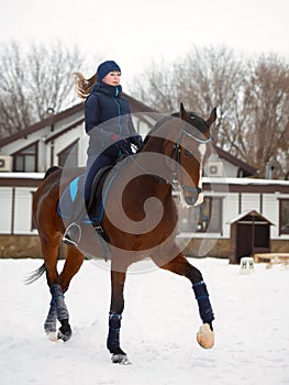 Equestrian country girl riding her bay horse in winter