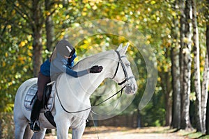 Equestrian lady riding horseback stroking white horse neck