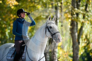 Equestrian lady riding white horseback in autumn alley