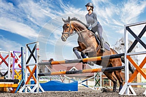 Equestrian sport. Show jumping competition. Young rider horseback girl jumping over an obstacle