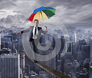 Equilibrist businessman walk on a rope with umbrella over the city. Concept of overcome the problems and positivity