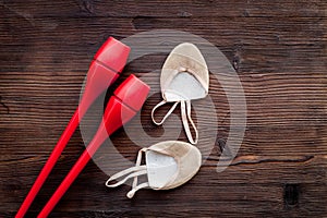 Equipment for rhythmic gymnastics. Clubs and gymnastics shoes on dark wooden background top view copy space