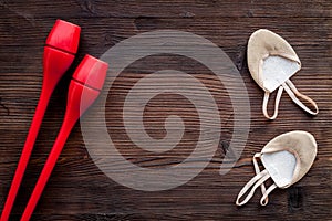 Equipment for rhythmic gymnastics. Clubs and gymnastics shoes on dark wooden background top view copy space