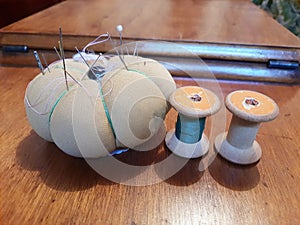 Equipment for sewing clothes, old wooden spool of thread, miniature cushion with threaded needles and pins,