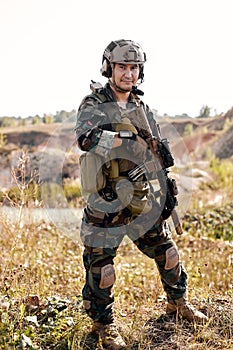 equipped camouflaged soldier man with rifle gun standing and posing outdoors, alone