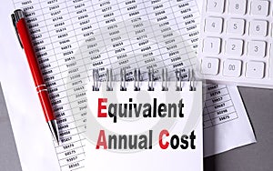 EQUIVALENT ANNUAL COST text on notebook with pen, calculator and chart on grey background