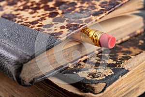 Eraser bound on a pencil and an old book. Writing accessories and books on an old table