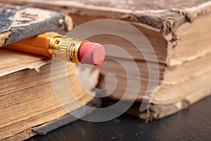 Eraser bound on a pencil and an old book. Writing accessories and books on an old table