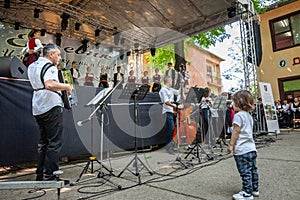 ERDEVIK, SERBIA - JUNE 3, 2023: toddler observing musicians and a group of children, boys & girls dancing a Serbian kolo in