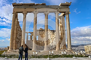 Erechtheion temple Acropolis Athens Greece with two tourists in front and the rooftops of Athens and a beautiful sky in the