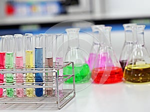 The Erlenmeyer conical Flasks and test tubes with rack on bench laboratory, with colorful solvent for testing indicator, titration