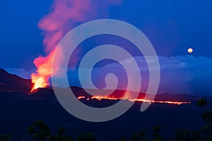 Errupting volcano in moonlit blue nightsky