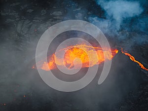 Erupted volcano and surroundings, boiling lava flowing, pull away drone shot