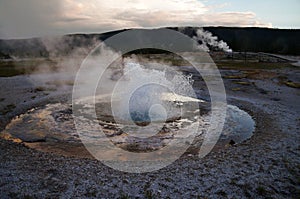 Erupting geyser: clouds reflected in a pond of hot spring run-off surrounded by white hydrothermal crust.
