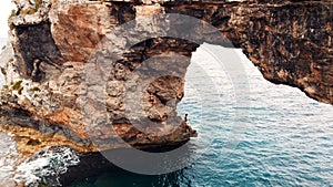 Es Pontas, turist climbling on Natural Rock Arch At The Coast Of Majorca Island, between Cala Santanyi and Cala